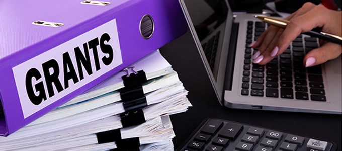 The word grants is written on a folder lying on documents on an office desk 
